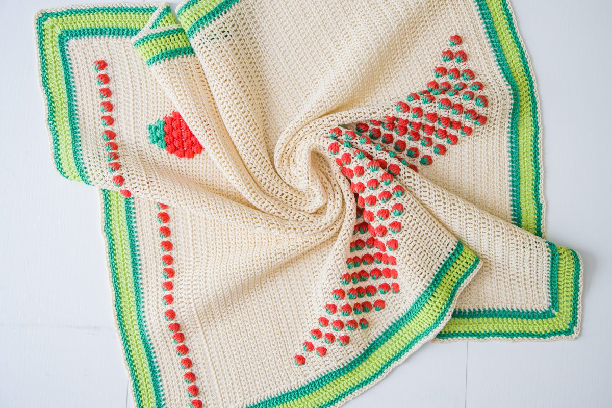 cream crochet blanket with strawberry detail and green edging