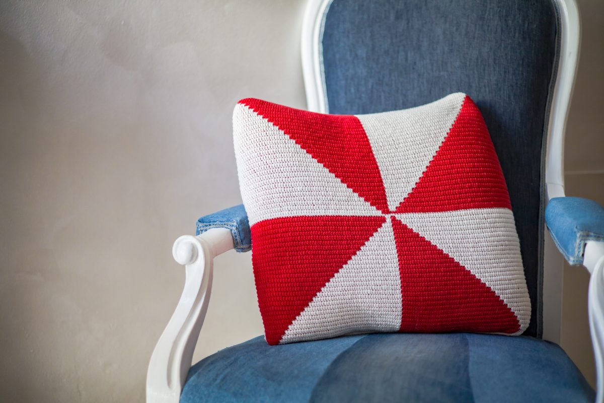 pinwheel red and white crochet pillow on a blue armchair