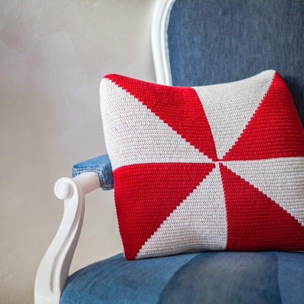 pinwheel red and white crochet pillow on a blue armchair